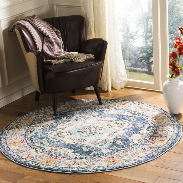 Safavieh Monaco Toria Traditional Area Rug, 3-foot round accent rug with navy and light blue Bohemian Persian design in durable polypropylene, placed on hardwood floor under a dark brown leather armchair with a beige herringbone throw, near a window with sheer curtains and a white vase with orange flowers, ideal for adding vibrant style to living rooms or reading nooks.