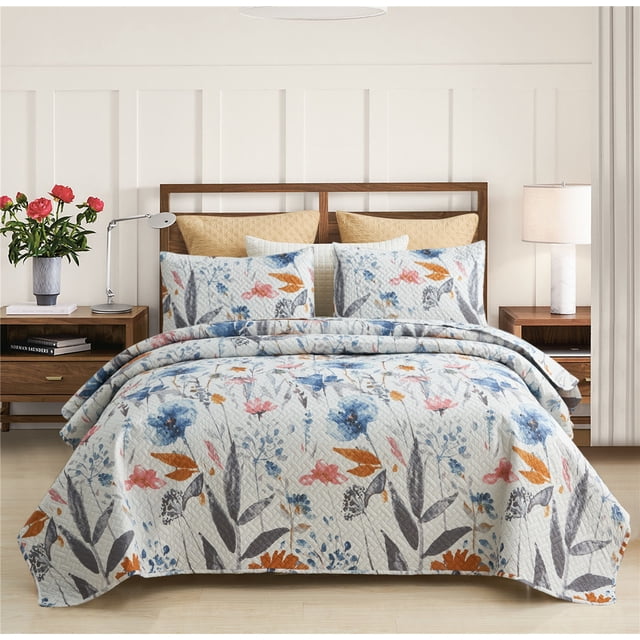 JML Quilt Set 3 Piece, Embossed Bedspread Bedding Set with 2 Shams, Queen, Colorful Floral. The image shows a queen-sized quilt set featuring a vibrant floral pattern in shades of blue, orange, and pink on a light background. The set includes a quilt and two matching pillow shams, displayed on a neatly made bed in a modern bedroom with wooden side tables, a lamp, and a vase of flowers.