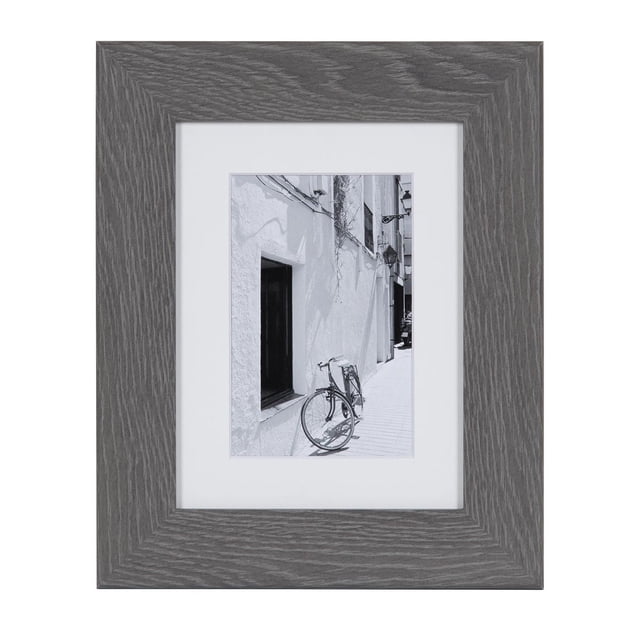 hometrends Museum Grey Picture Frame with a wide grey wood grain profile and white mat holding a black and white photo of a bicycle leaning against a white stucco wall, fits 4x6 inch photos with mat or 6x8 inch without, includes hanging hardware for vertical or horizontal wall display and an easel for tabletop use, suitable for creating a gallery wall