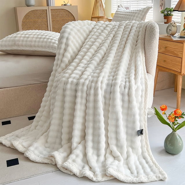 Dvkptbk Woolen Blanket Soft Bubble Fleece Blanket draped over a chair in a cozy bedroom. The blanket, made from double-sided velvet, features a white solid color and textured bubble fleece design. Measuring 100x150cm, it is warm, breathable, and suitable for all-season use. Perfect for naps, reading, or watching TV, it complements the room's decor, which includes a bed, wooden furniture, and floral accents.