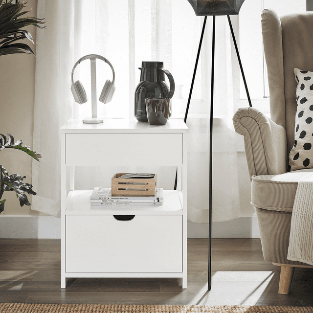 SoBuy Beside Table with Drawers, Night Table Stand Lamp Table End Table Side Table, White FRG258-II-W. A white MDF bedside table featuring a modern design with two drawers and an open shelf for storage. Dimensions are 17.72 inches long, 14.96 inches wide, and 21.65 inches high (45 x 38 x 55 cm). Positioned in a cozy living room setting with a beige armchair, a floor lamp, and decorative items like headphones and a coffee pot on the table.