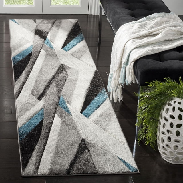 Safavieh Hollywood Jennifer Tapis Abstrait pour Aire avec design Géométrique Moderne Mi-Siècle en Gris, Noir, Blanc et Bleu, Fabriqué en Polypropylène Synthétique durable, Placé sur Plancher de Bois Franc Foncé à Côté d'Un Banc Capitonné Noir avec un Jeté à Franges Blanc et Bleu et un vase en Céramique Blanc avec Feuillage Vert, Convient pour Ajouter un style Contemporain aux Espaces de Vie.