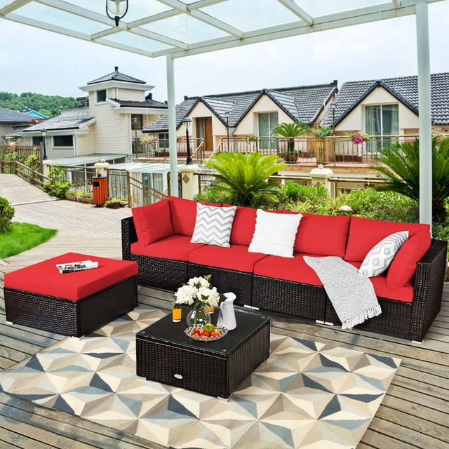 Costway Ensemble de Meubles d'Extérieur en Rotin pour Patio 6 Pcs, Canapé Sectionnel Rembourré Rouge, Comprenant Deux Canapés d'Angle, Deux Canapés Sans Accoudoirs, un ottoman et une table Basse en Verre Trempé. l'Ensemble Est Conçu avec un Cadre en Acier Enduit de Poudre et un Osier en Rotin PE Résistant aux Intempéries pour la Durabilité. des Coussins Rouges Épais Offrent du Confort, et la Conception Modulaire Permet Diverses configurations. Exposé sur un Patio en Bois avec un Tapis Géométrique et Entouré de Verdure.