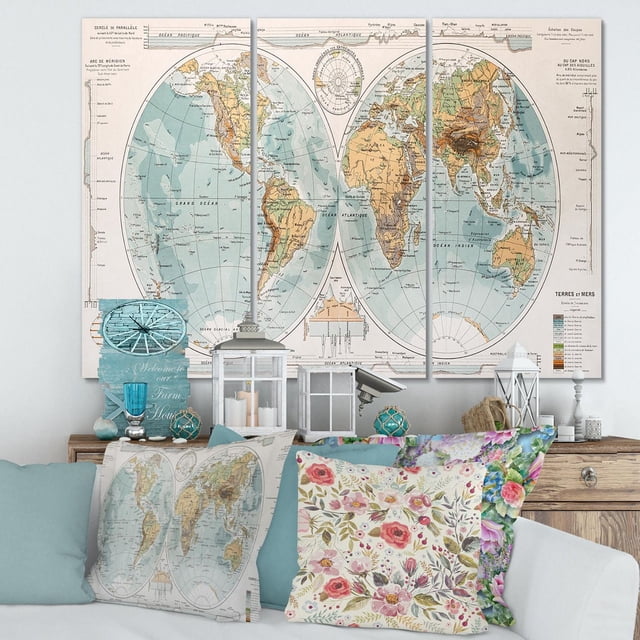 Designart Ancient Map of The World II Canvas Wall Art featuring a three-panel vintage world map in blue and brown tones, printed on premium cotton canvas with fade-resistant ink. The gallery-wrapped canvas is displayed above a wooden console with decorative pillows, including one with a matching map print and floral designs, ideal for rustic home décor.