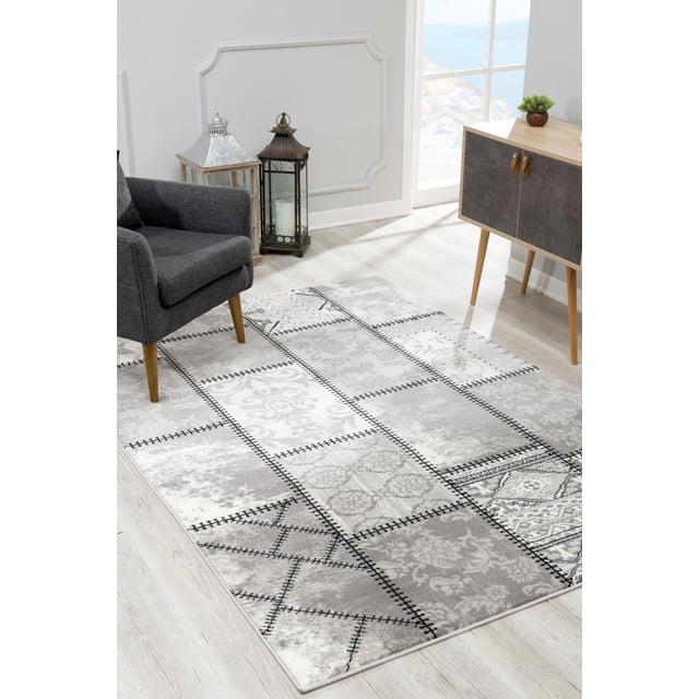 Rug Branch Montage Modern Abstract Indoor Area Rug with a patchwork of vintage and abstract grey and white motifs outlined by black stitched borders, displayed on light wood flooring under a dark grey armchair near decorative lanterns and a wooden cabinet, ideal for living rooms, bedrooms, or hallways.