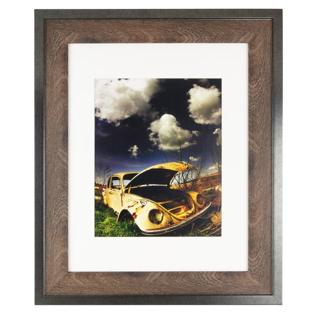 kieragrace Railtown Benton Frame – 11-Inch by 14-Inch, Matted for 8-Inch by 10-Inch, Iron Grey, Walnut Wood displaying a front-facing view of a photo frame with an iron grey outer edge and walnut wood inner trim. The frame holds a matted photo of a weathered yellow vintage car with its hood open, set outdoors under a partly cloudy sky. It features sawtooth hangers for horizontal or vertical wall mounting and an easel back for tabletop display, suitable for industrial and rustic home décor.