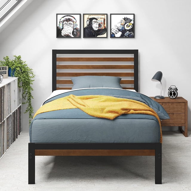 Zinus Kai 35 inch Bamboo and Metal Platform Bed Frame, No Box Spring Required, Twin, front view showing a modern platform bed with black steel frame and natural bamboo slats on headboard and footboard, dressed with blue bedding and a yellow throw, in a bright bedroom with white walls, three framed monkey art prints above, a wooden nightstand with a black lamp and alarm clock, and a white shelving unit with plants and vinyl records on the left.