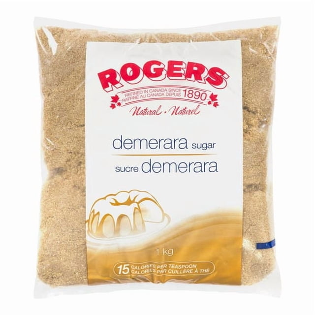 Rogers Sugar Brown Demerara 1Kg/2.20 LBS in a clear plastic bag with bold red branding and text. The natural raw cane sugar features large golden crystals and rich caramel notes, ideal for baking, coffee, tea, and cocktails. The front of the bag highlights its 15 calories per teaspoon and trusted Rogers quality.