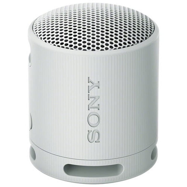 Sony SRS-XB100 waterproof Bluetooth wireless speaker in light grey, showcasing a compact cylindrical design with a textured finish and perforated grille. This portable speaker is IP67-rated for waterproof and dustproof durability, includes Bluetooth connectivity, and offers up to 16 hours of battery life. UV protection enhances outdoor durability, making it suitable for travel or outdoor activities.