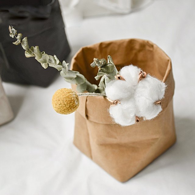 Washable Kraft Paper Bag Plant Flowers Pots Multifunction Home Storage Bag in brown, shown holding decorative cotton stems and a yellow billy ball flower. Made from tear-resistant, washable kraft paper with a nostalgic metallic finish. Suitable for use as a plant pot cover, storage for craft materials, jewelry, or small household items. Dimensions approximately 8 x 8 x 15 cm.