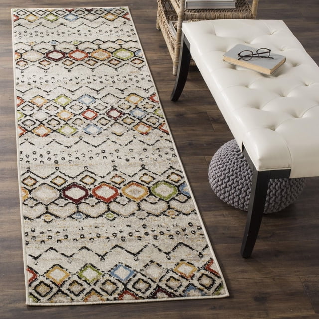 SAFAVIEH Amsterdam Gladwin Geometric Area Rug runner with a beige background featuring multicolored diamond and tribal patterns in red, green, blue, orange, and black, power-loomed from durable synthetic yarns, placed on dark hardwood flooring beside a white tufted bench and wicker chair, suitable for rustic-chic décor and hallway use.