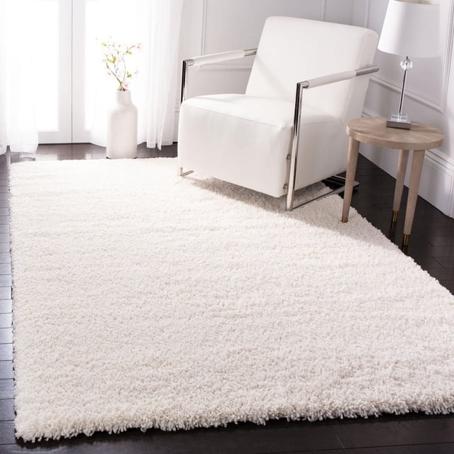 SAFAVIEH Fontana Jamie Tapis Shag Uni en Peluche Blanc Cassé avec pile Peluche de 2 Pouces, Posé sur Plancher de Bois Franc Foncé à Côté d'Un Fauteuil Moderne Blanc avec Accoudoirs Chromés, à Côté d'Une table d'Appoint Ronde en Bois avec Lampe et un vase Blanc avec des Fleurs Près d'Une Fenêtre à Voilage, Idéal pour Ajouter Douceur et Chaleur aux Salons.