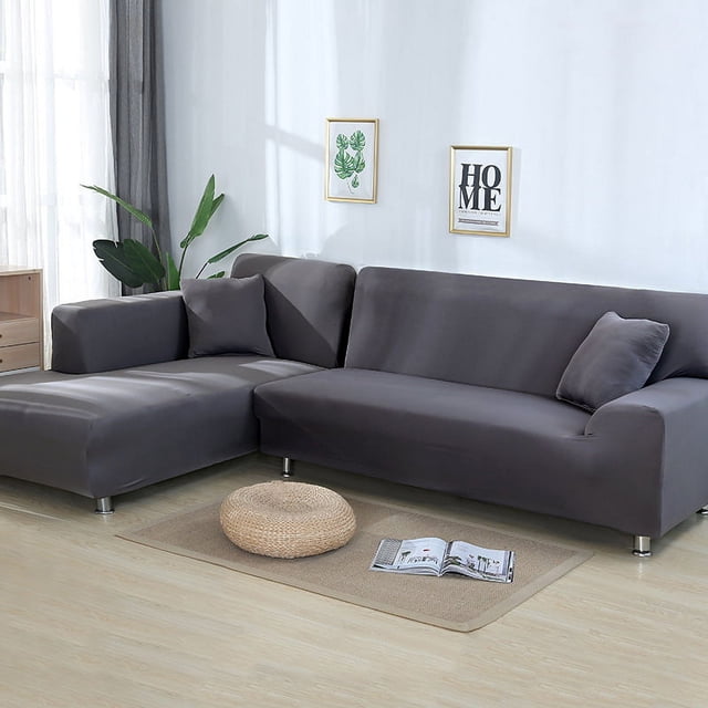 Labymos Elastic Sofa Cover All-Inclusive Universal Cover for L-shaped concubine and leather sofas in a dark grey colour. The cover is shown fitted on an L-shaped sofa in a modern living room with light wood flooring, a beige rug, and minimalist wall decor.