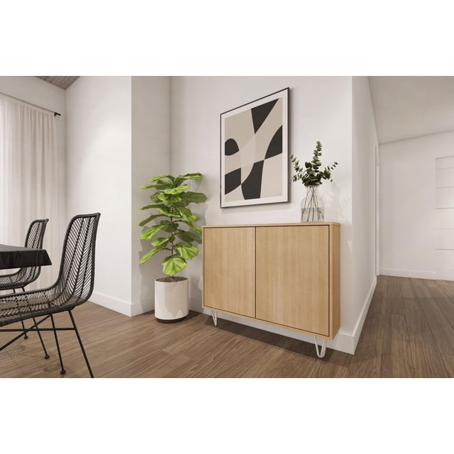 Nexera Slim 2-Door Storage Accent Cabinet in light wood finish placed in a modern dining area corner, styled with green plants and abstract artwork.