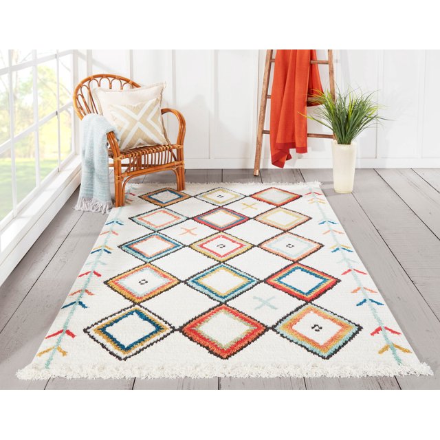 ECARPET Vivi Contemporary Area Rug with a white base and southwestern diamond patterns in coral red, aqua blue, yellow, and black, placed on light grey wood flooring beside a rattan chair with a beige geometric pillow and light blue throw, near a wooden ladder with an orange blanket and a potted green plant, ideal for living rooms, bedrooms, or hallways.