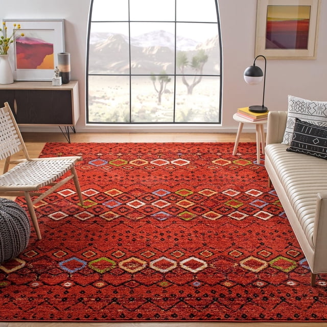 SAFAVIEH Amsterdam Gladwin Tapis Géométrique Mettant en Vedette une pile Ton Terre Rouge avec des Motifs Tribaux Multicolores en Losanges en Bleu, Vert, Blanc et orange. Tissé Mécaniquement à Partir de Fils Synthétiques Durables, Ce Tapis d'Accent Est Exposé sur un Plancher en Bois dans un Salon avec une Chaise Tissée, un sofa beige avec des Coussins à Motifs, et une table d'Appoint avec une Lampe Moderne, sous une Grande Fenêtre Arquée Surplombant un Paysage Désertique. Il Convient Aussi pour Ajouter une Déco Rustique Chic à Divers Espaces Intérieurs