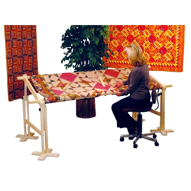 American Legacy Cadre de Courtepointe par Keepsake Quilting, Cadre de Courtepointe en Bois Pleine Grandeur Ajustable Montré en Utilisation avec une Courtepointe Multicolore. le Cadre Mesure 24x90 Pouces et Peut Être Réduit à 24x45 Pouces pour des Projets Plus Petits. une Femme Est Assise, Courtepointe Confortable avec le Cadre Ajusté pour la Hauteur et l'Angle. la construction en Bois Massif Non Fini Est Robuste, avec des Tiges Détachables pour un Rangement Facile. les Courtepointes et les Arrière-Plans Décoratifs Sont Visibles dans le Cadre.