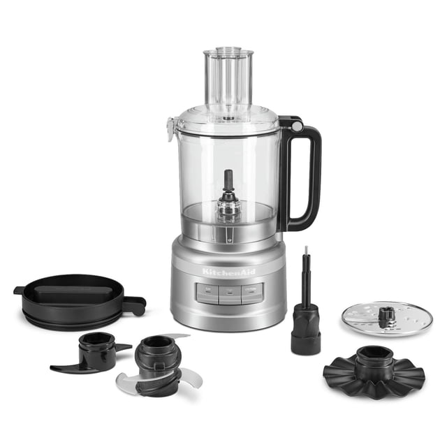 KitchenAid® Robot Culinaire de 9 Tasses avec Bol de Travail Transparent de 9 Tasses et Poignée Noire, base Argentée avec Trois Boutons de Vitesse, et Accessoires Inclus : Quatre Lames Polyvalentes pour Hacher et Émincer, Lame à Pâte pour Pétrir, Fouet pour Fouetter, Disque Réversible pour Trancher/déchiqueter, et Couvercle de Réfrigérateur pour Rangement, Illustré sur un Fond Blanc.