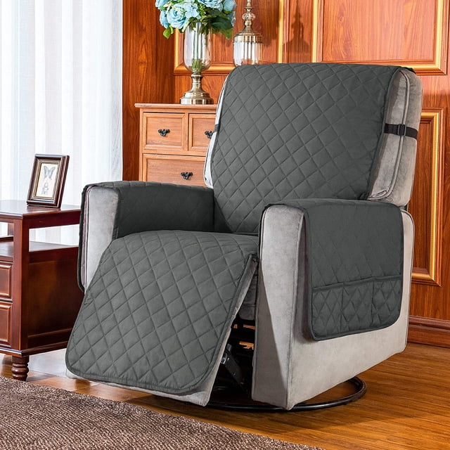 Subrtex Reversible Recliner Chair Cover in grey, displayed on a recliner in a cozy living room with wooden accents and floral decor. The cover has a quilted pattern, side pockets for storage, and adjustable elastic straps for a snug fit. Made from durable 100% microfiber fabric, it protects furniture from spills, stains, and wear. Available in small (25-inch seat width) and large (28-inch seat width) sizes.