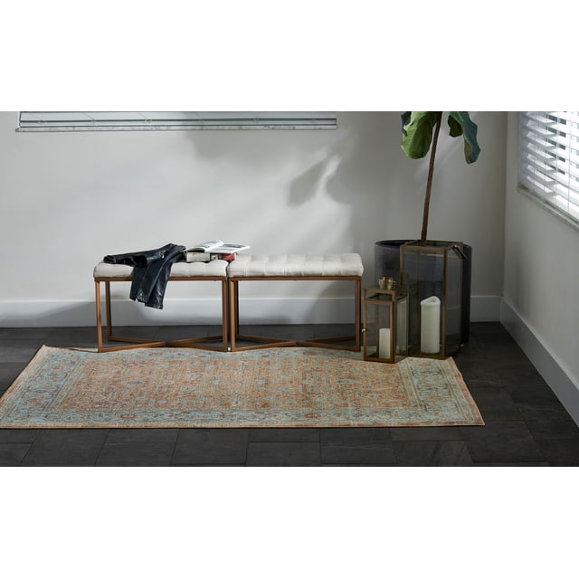 ECARPET Hailey Traditional Area Rug for Living Room, Bedroom, Dining Room, Entrance, Hallway and More with an orange and blue ornate pattern on a dark tile floor beneath a beige tufted bench with bronze metal legs, beside two brass-framed glass lanterns holding white candles and a large potted plant in a bright room with white walls and blinds. This rug is also suitable for use as a decorative accent in entryways or under vintage dining sets.