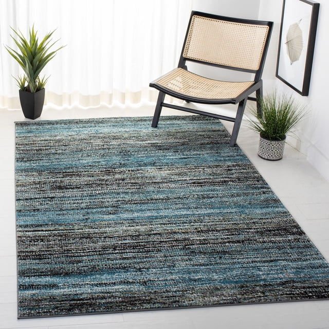 SAFAVIEH Porcello Manus Contemporary Area Rug with a soft, texture-rich pile in blended blue, gray, and black tones, placed on light hardwood flooring beside a black wooden chair with woven cane seat and backrest, accented by two potted plants and framed abstract wall art, suitable for casual living rooms or bedrooms.