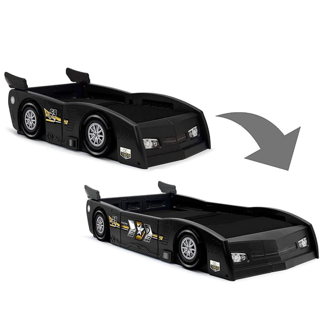 Delta Children Grand Prix Race Car Toddler & Twin Bed in black, designed to resemble a race car with an aerodynamic spoiler, 3D accents, and decals highlighting headlights, wheels, and exhaust. The image shows the bed in both toddler and twin configurations, showcasing its convertible design. Made from durable molded plastic, it includes panels for easy transformation and ensures safety with a low mattress position and secure guardrail sides. Ideal for toddler and twin-sized mattresses.