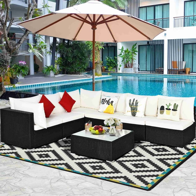 Costway 7PCS Patio Rattan Sofa Set Sectional Conversation Furniture Set Garden Beige arranged poolside. Features four armless sofas, two corner sofas, and a coffee table with a tempered glass top. Beige cushions and pillows rest on a black PE wicker frame, set on a patterned outdoor rug under a beige umbrella. Ideal for outdoor sectional seating in gardens, patios, or poolside areas.