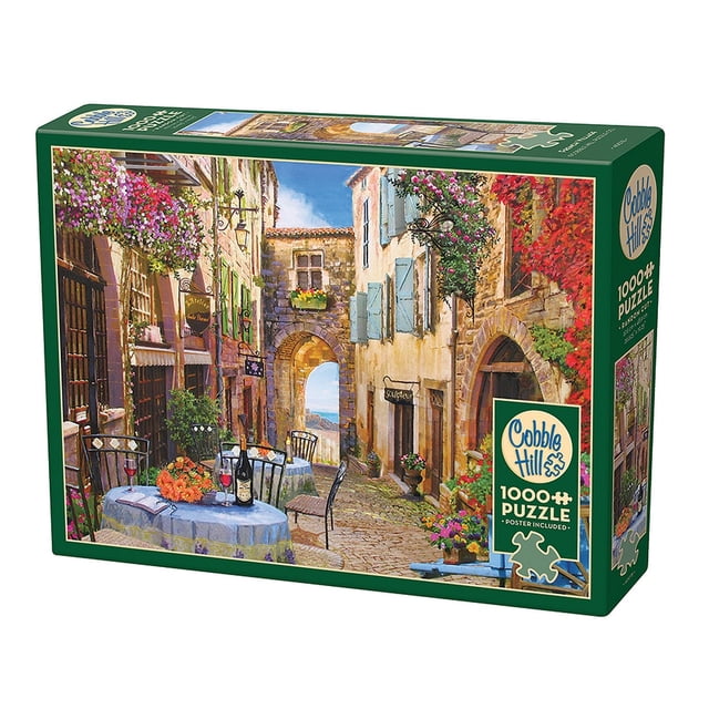Cobble Hill Jigsaw Puzzle - French Village, 1000 Piece Puzzle showcasing a picturesque French village scene with cobblestone streets, vibrant flowers, and outdoor tables set with wine and cheese. The puzzle features random-cut pieces, a linen paper finish for reduced glare, and eco-friendly materials made in North America. Assembled size is 26.625 x 19.25 inches.