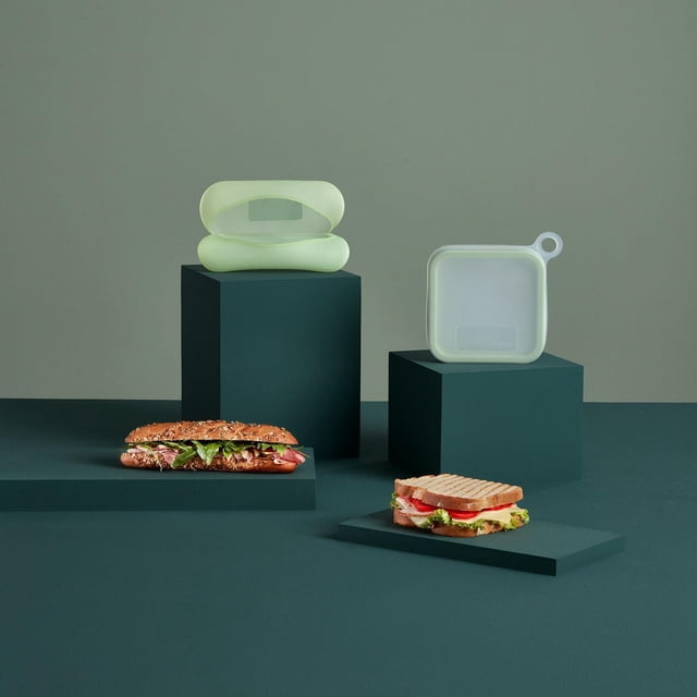 Lekue Ensemble de Contenants de Rangement Alimentaire en Silicone Réutilisables pour Sandwichs et Baguettes, Présenté sur des Plateformes Vert Foncé avec Deux Sandwichs, Comprenant un Étui à Baguette en Silicone Souple Translucide Ouvert et un Étui à Sandwich Carré avec Poignée en Boucle, Convient au Rangement de lunch Écologique, Ajustable et Gain de Place.