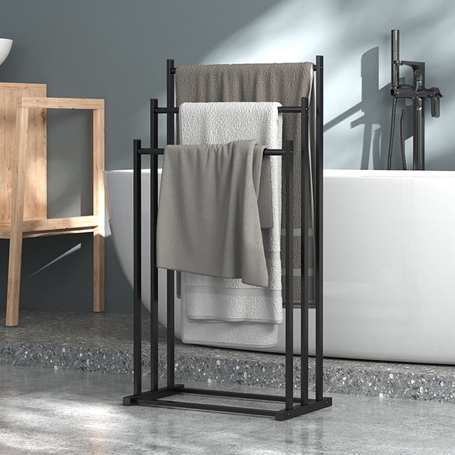 Cameland Floor Standing Towel Rack with three-tiered vertical design made of black iron, shown in a modern bathroom setting. The rack features staggered height bars for efficient towel drying and storage. Its compact and lightweight structure includes a widened base for stability and enhanced load-bearing capacity. Positioned near a white bathtub with towels draped over each tier.