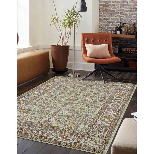 ECARPET Hailey Traditional Area Rug in sage with an ornate floral pattern on dark hardwood floors, shown with a brown leather swivel chair with beige cushion, a tall potted plant, a stainless steel floor lamp, and a brick accent wall with a shelf holding bottles and decor, ideal for classic or vintage-style living spaces.
