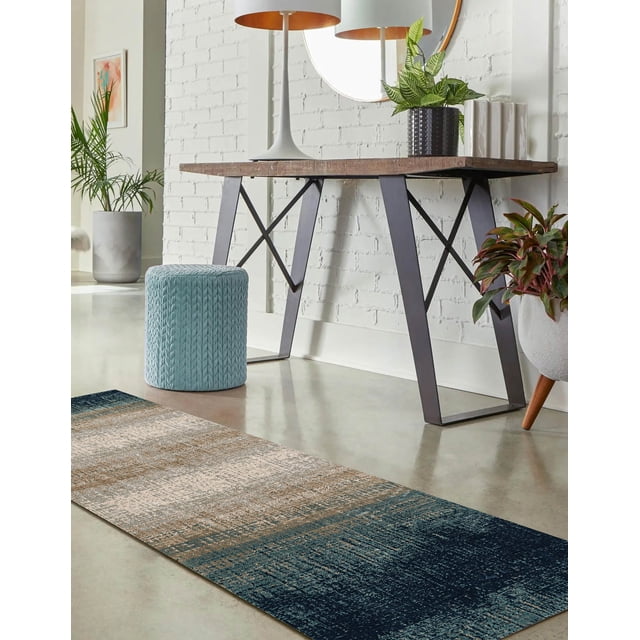 ECARPET Sable Contemporary Runner Rug on a polished concrete floor with a textured gradient pattern in navy blue, beige, and brown tones. Positioned near a wooden console table with black metal legs, white lamp, round mirror, and potted plants, the rug suits hallways, entrances, or living rooms and is often used to add warmth and style to narrow spaces.