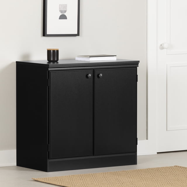 South Shore Morgan Small 2-Door Storage Cabinet in pure black with a contemporary style, featuring two doors with small round handles and an adjustable shelf inside, suitable for entryway or home office storage, shown in a minimalist room with a beige rug and framed wall art.