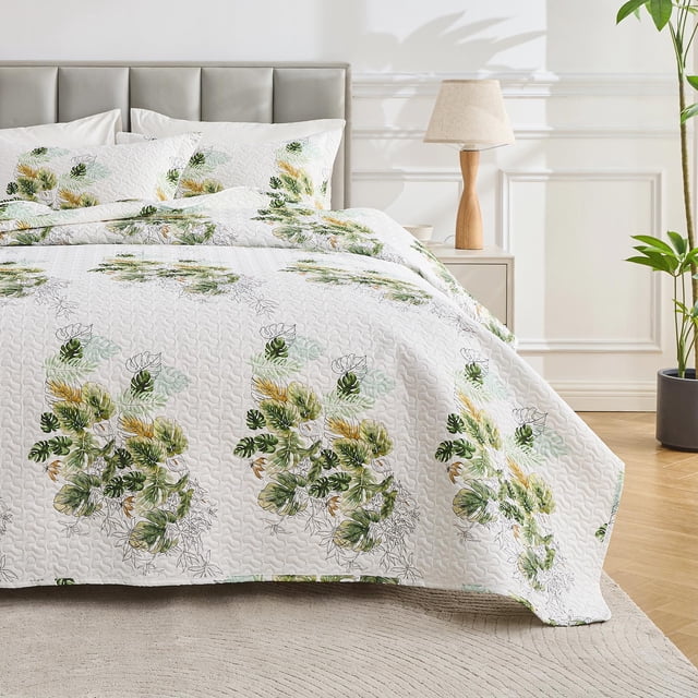 Hitime Luxury Printed Quilt Set Queen Size displayed in a bedroom setting. The lightweight comforter set features a white base with vibrant green and yellow floral patterns, adding a touch of nature-inspired elegance. The quilted bedding set includes an oversized bedspread and two matching pillowcases, crafted from 100% brushed microfiber for softness and durability. The medium-weight design with heavier-than-average microfiber filling ensures comfort for all seasons. The bed is styled with a grey upholstered headboard, a wooden nightstand with a lamp, and a potted plant in the background, creating a cozy and inviting atmosphere.