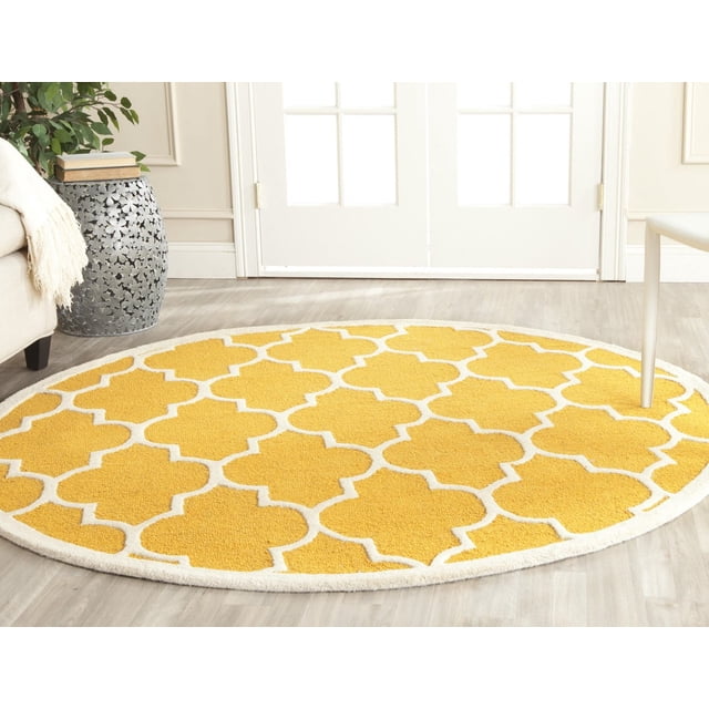 Safavieh Cambridge Kevin Geometric Area Rug, round hand-tufted wool rug with yellow and white geometric pattern on light hardwood floor in a bright room with white French doors, beige sofa, and metal side table with books and plant, ideal for adding modern American style to home decor.