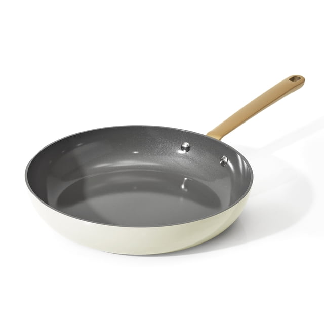 Beautiful by Drew Barrymore 12 inch ceramic non-stick fry pan with beige exterior and dark gray ceramic interior, featuring a long tan handle with riveted attachment, compatible with all stovetops including induction and oven safe to 500°F, often used for sautéing vegetables evenly.