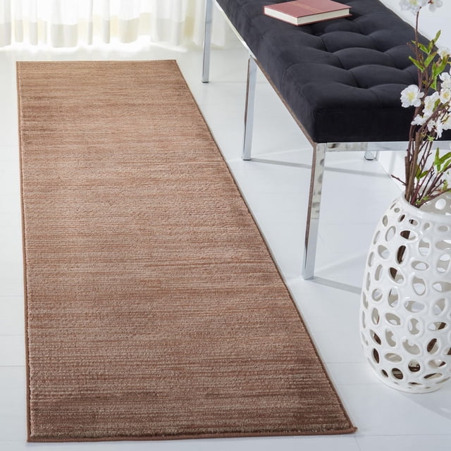Safavieh Vision Adrasteia Overdyed Solid Area Rug runner in warm brown with soft textured pile, placed on a white floor next to a black tufted bench with chrome legs and a white ceramic vase with flowers, suitable for enhancing texture in modern living rooms or hallways.