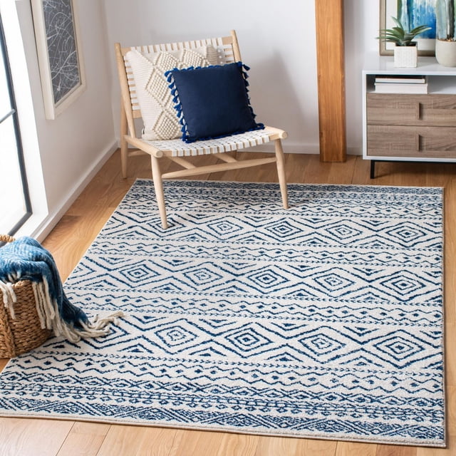 SAFAVIEH Tulum Merletta Moroccan Geometric Area Rug in blue and cream with diamond and linear patterns, placed on light hardwood flooring in a bright room with a natural wood woven chair holding cream and navy blue pillows and a basket with a blue and cream throw, suitable for enhancing boho-chic décor and adding comfort underfoot.