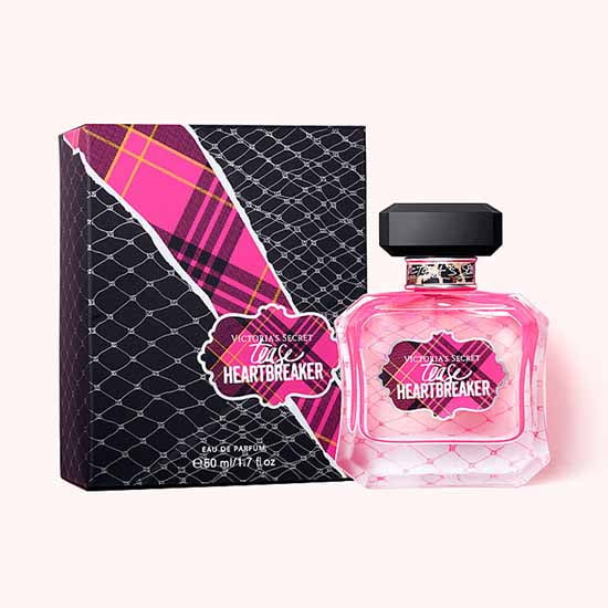 Victoria's Secret Tease Heartbreaker EDP pour Elle 50 ml Bouteille de Parfum pour Femme Exposée à Côté de Sa Boîte Assortie. la Bouteille Présente un design en Verre Rose avec un Bouchon Noir, pendant Que la Boîte Met en Valeur un Motif Audacieux à Carreaux et en Maille Inspiré des Tendances des Podiums d'Automne 2019.
