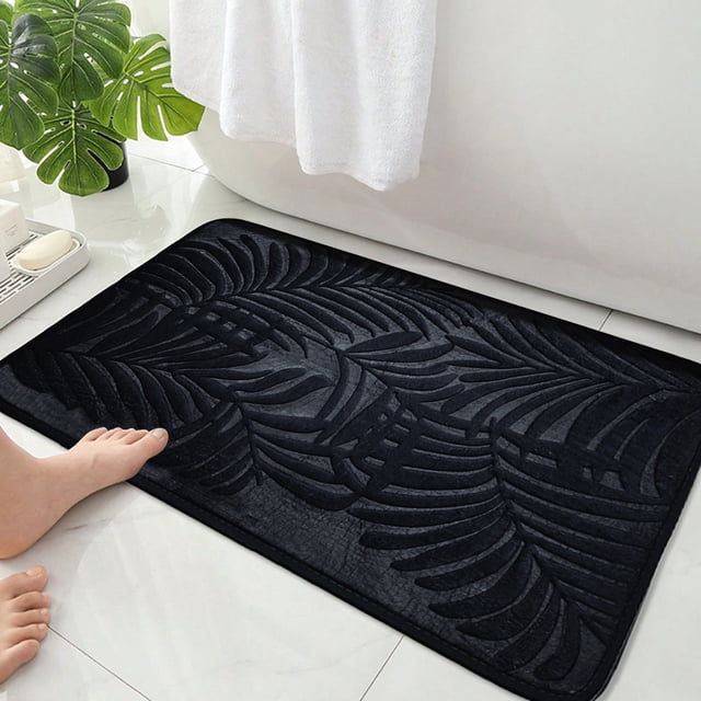EGNMCR Bathroom Water Absorbent Door Mat in black, measuring 40x60cm (15.74x23.62in). This quick-dry entry mat features a solid color design with a textured leaf pattern, crafted from polyester with a rubber non-slip backing. Ideal for use in bathrooms, shower rooms, or as an entrance rug, it offers excellent water absorption and rapid drying. The mat is shown placed on a tiled bathroom floor near a bathtub, with a white towel and green plant in the background.