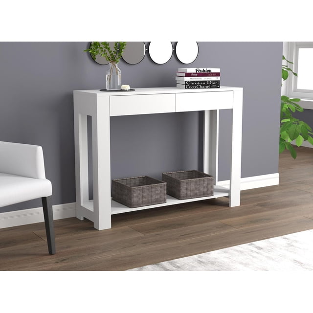 Safdie & Co. Console Table 40" White With 2 Drawers, modern white console table with a spacious top holding stacked fashion books and a glass vase with greenery, featuring two wide drawers and an open lower shelf with two woven storage baskets, suitable as entryway furniture or an accent table, set against a gray wall with round mirrors and wood flooring.