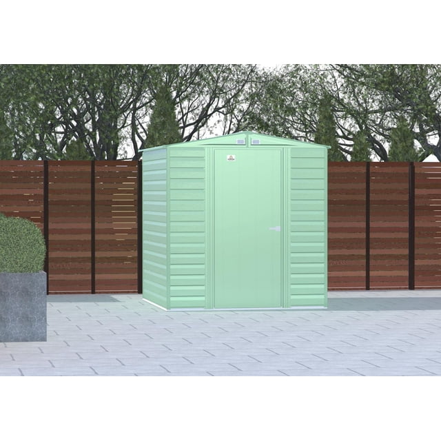 Arrow Select Remise de Rangement en Acier Remise de Rangement en Acier, 6x7, Vert Sauge, Vue Frontale avec Panneaux de Parement Horizontaux et Toit en Pente avec Évents Intégrés, Située sur une Cour Arrière Pavée avec Clôture en Bois et Arbres, en Acier Galvanisé Résistant à la Corrosion, Convient au Rangement Extérieur.