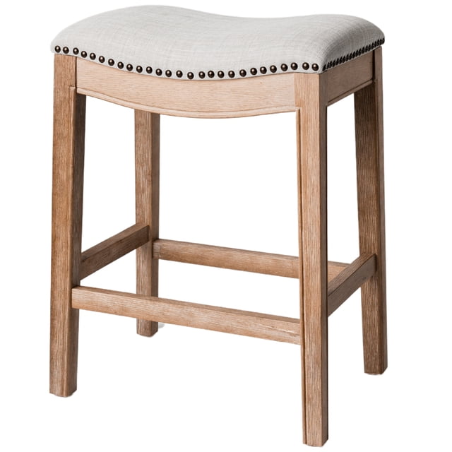 Maven Lane Adrien Saddle Counter Stool in Weathered Oak Finish with Sand Color Fabric Upholstery. This backless stool features a contoured saddle cushion with hand-applied nailhead trim, kiln-dried hardwood construction, and a hand-brushed wood finish. Designed for counter height seating, it measures 19.7 inches wide, 14.2 inches deep, and 26 inches high. The neutral sand fabric and organic wood grain make it a versatile addition to various kitchen or dining aesthetics.