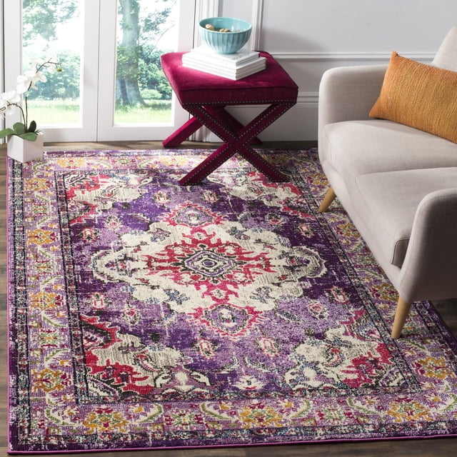 Safavieh Monaco Toria Traditional Area Rug with a Bohemian-chic Persian design in purple, red, cream, and yellow, power-loomed polypropylene with mixed loop pile, displayed in a living room with a beige sofa and burgundy velvet ottoman, ideal for adding vibrant style to home decor.