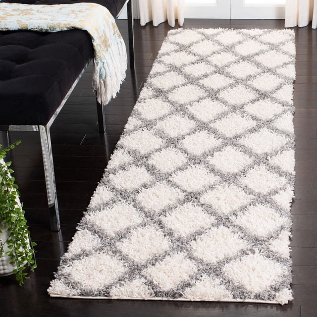 Safavieh Dallas Jerrie Tapis Coureur à Motif Géométrique Shag pour Aire, Présentant un Motif de Losanges Blanc et Gris avec des Fibres Synthétiques Douces et Denses, Conçu pour la Durabilité dans les Espaces Domestiques Ou de Bureau Très Passants, Exposé sur un Plancher de Bois Franc Foncé à Côté d'Un Banc Noir avec un Jeté Bleu Pâle et beige.