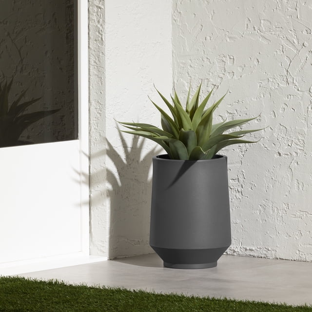 Jardinière de la collection Dalya South Shore en Polyéthylène Gris Foncé Mat avec une Forme Cylindrique Effilée Tenant une Succulente Verte, Posée sur un Plancher de patio Gris Pâle contre un Mur Blanc Texturé Près d'Une Porte Blanche avec Panneau en Verre, Convient pour une Utilisation Intérieure Ou Extérieure.