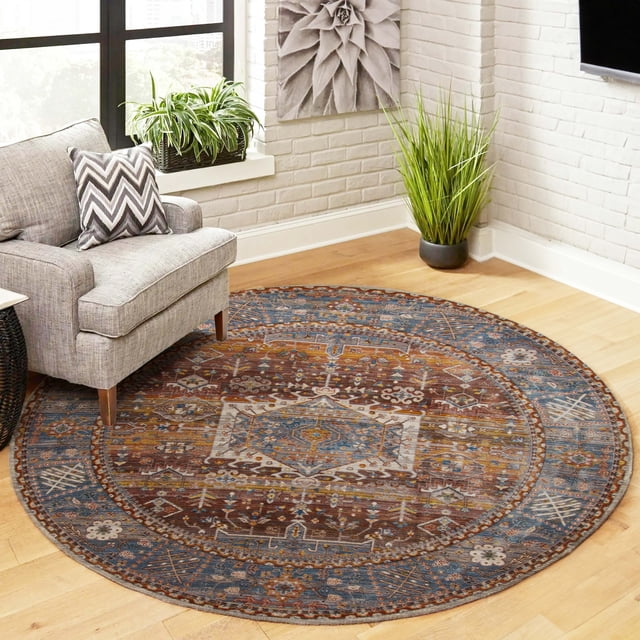 ECARPET Dulce Traditional Area Rug, a round low-pile polyester rug with a multi-color Turkish-inspired pattern in blue, brown, and beige tones, placed on a light hardwood floor beside a gray upholstered armchair with a chevron pillow, near white brick walls and green plants, ideal for living rooms, bedrooms, or hallways.