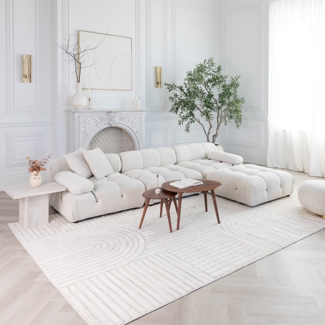Rug Branch Astra Modern Indoor Area Rug, Cream Beige, Geometric - cream beige geometric area rug placed in a bright living room featuring a tufted cream sectional sofa, two wooden mid-century coffee tables, a white side table with dried flowers, and a large green potted plant near a white decorative fireplace, ideal for high-traffic areas including kitchen and dining rooms.