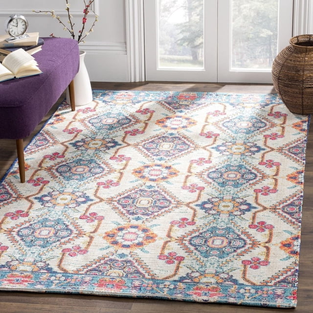 Safavieh Saffron Ira Floral Bordered Area Rug featuring a colorful geometric and floral pattern in blue, pink, orange, and cream on soft cotton, placed on hardwood flooring near a purple bench and natural light from glass doors. This hand made rug with a distressed border adds a quaint accent to home decor and is suitable for use as a soft floor covering in living spaces.