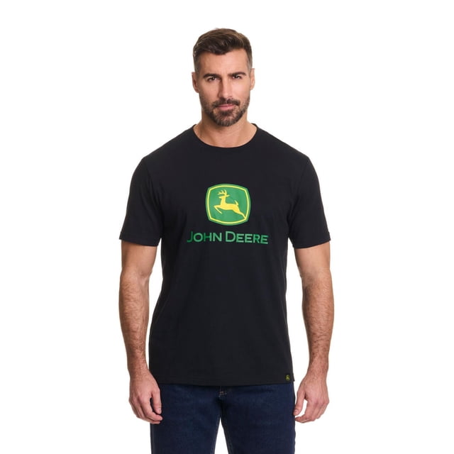 John Deere Men’s Logo Graphic Short Sleeve Tee in black jersey fabric featuring the green and yellow John Deere deer logo and text printed on the chest, shown front-facing on a male model wearing dark blue jeans, suitable for casual wear or pairing with John Deere shorts or pants.